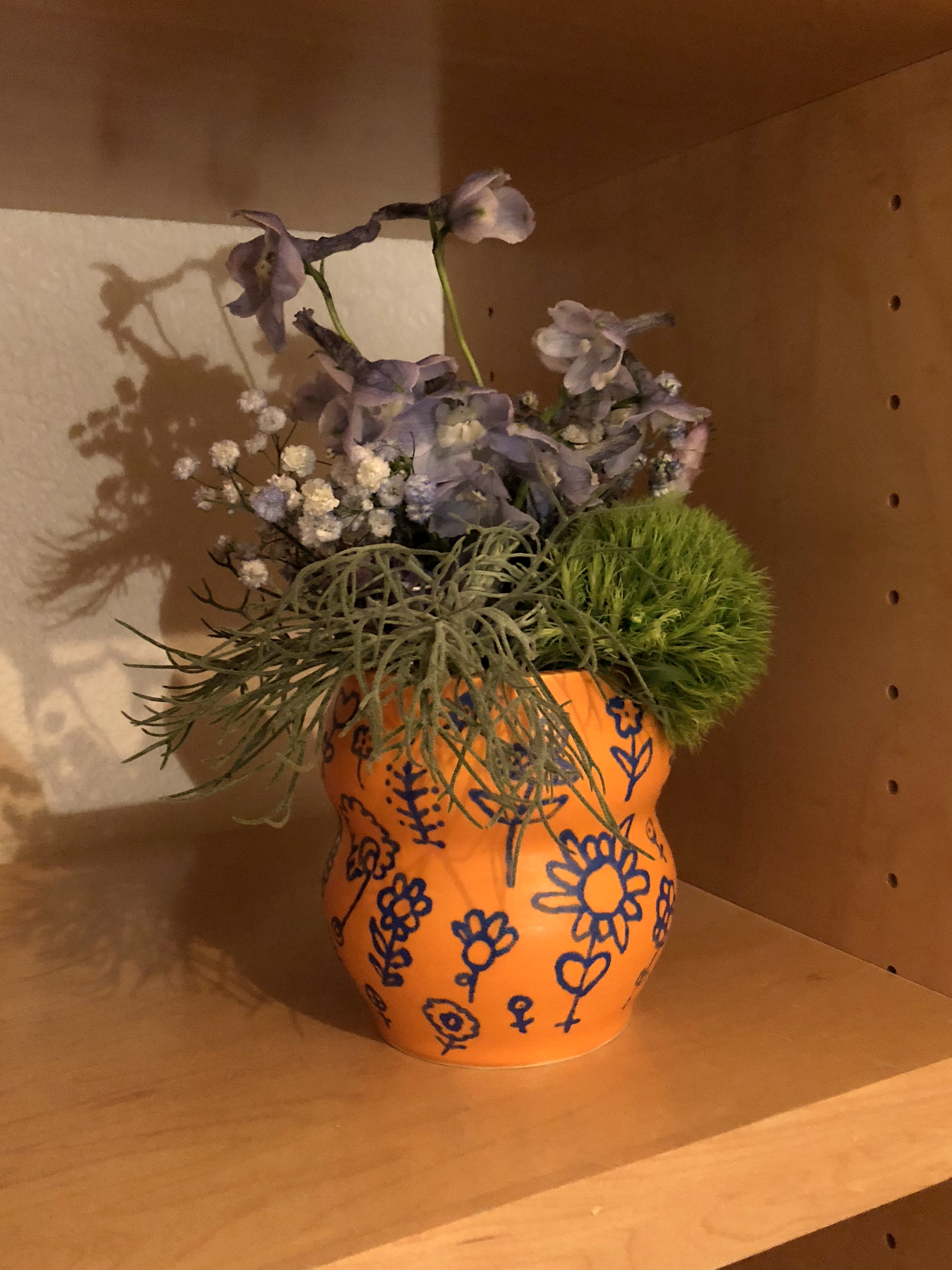 Orange ceramic vase with drawings on it holding colorful flowers